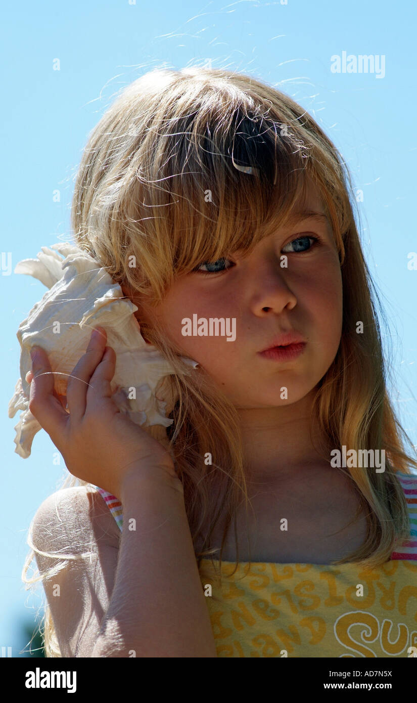 Little girl holding a seashell to her ear Listens to the sound of the seaside Stock Photo
