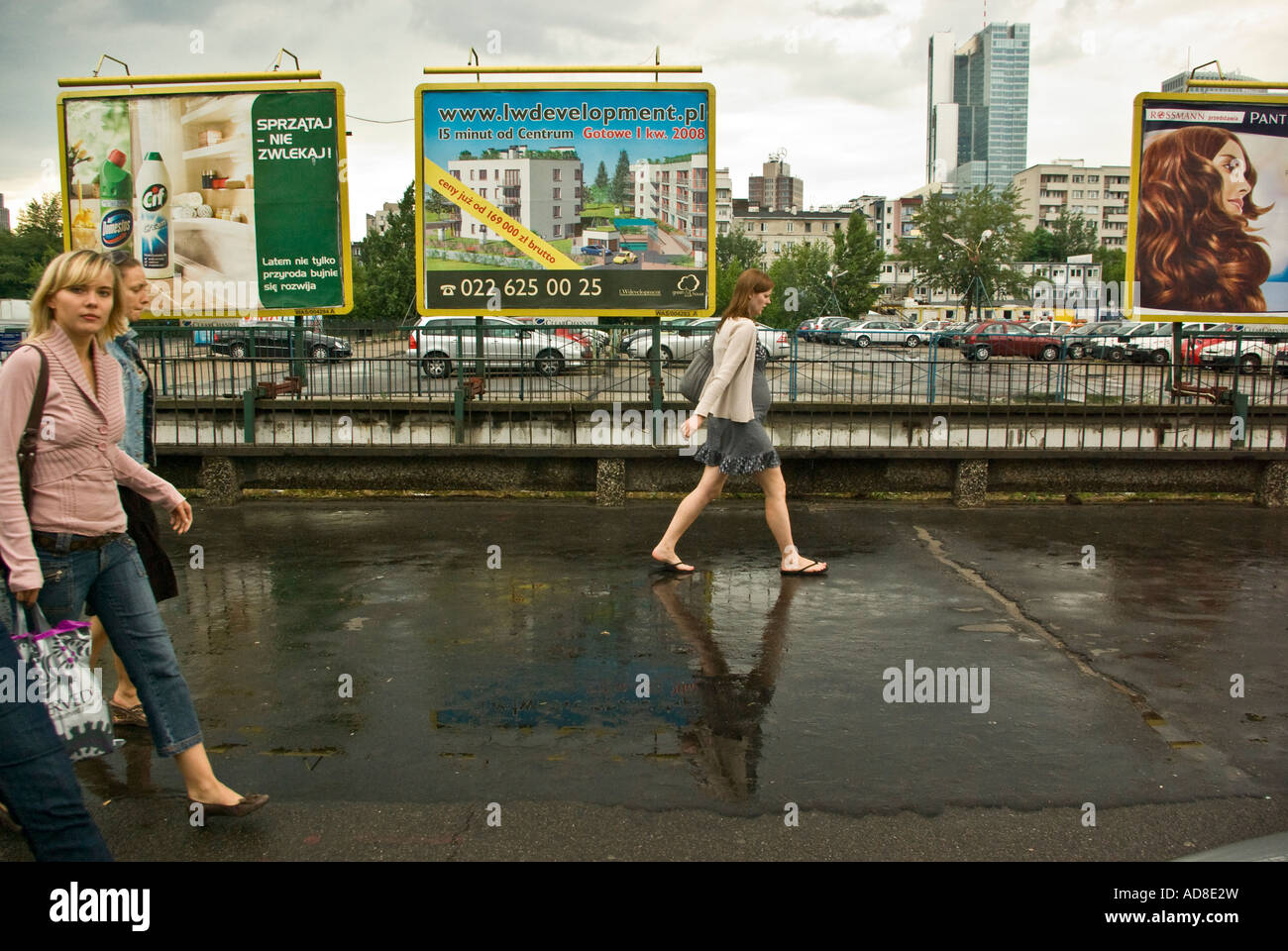 Three young women walking past billboards on rainy day in downtown