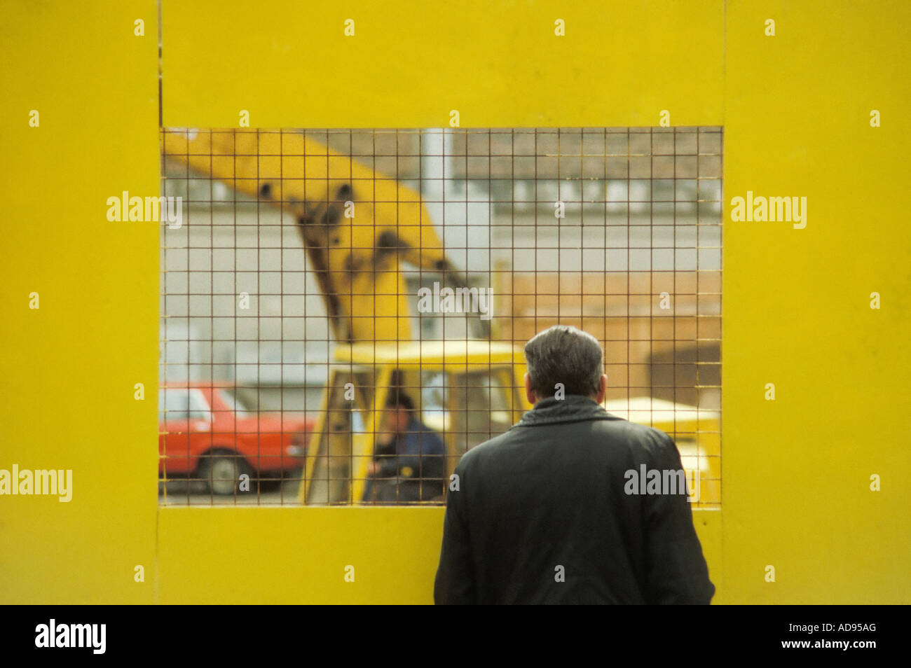 Old man watches building construction work through barrier Stock Photo
