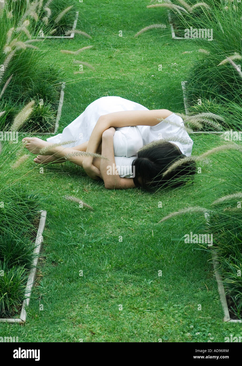 Woman curled up in fetal position on grass Stock Photo