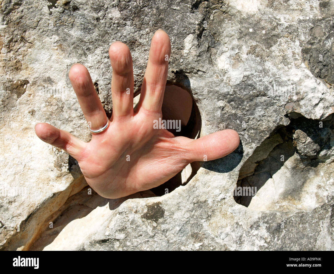 hand with straddeled fingers through a hole in a stone Stock Photo