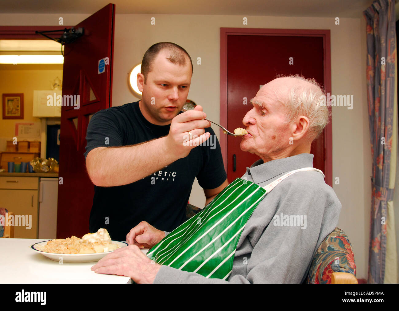 Care staff Eastern European helping elderly man with feeding in