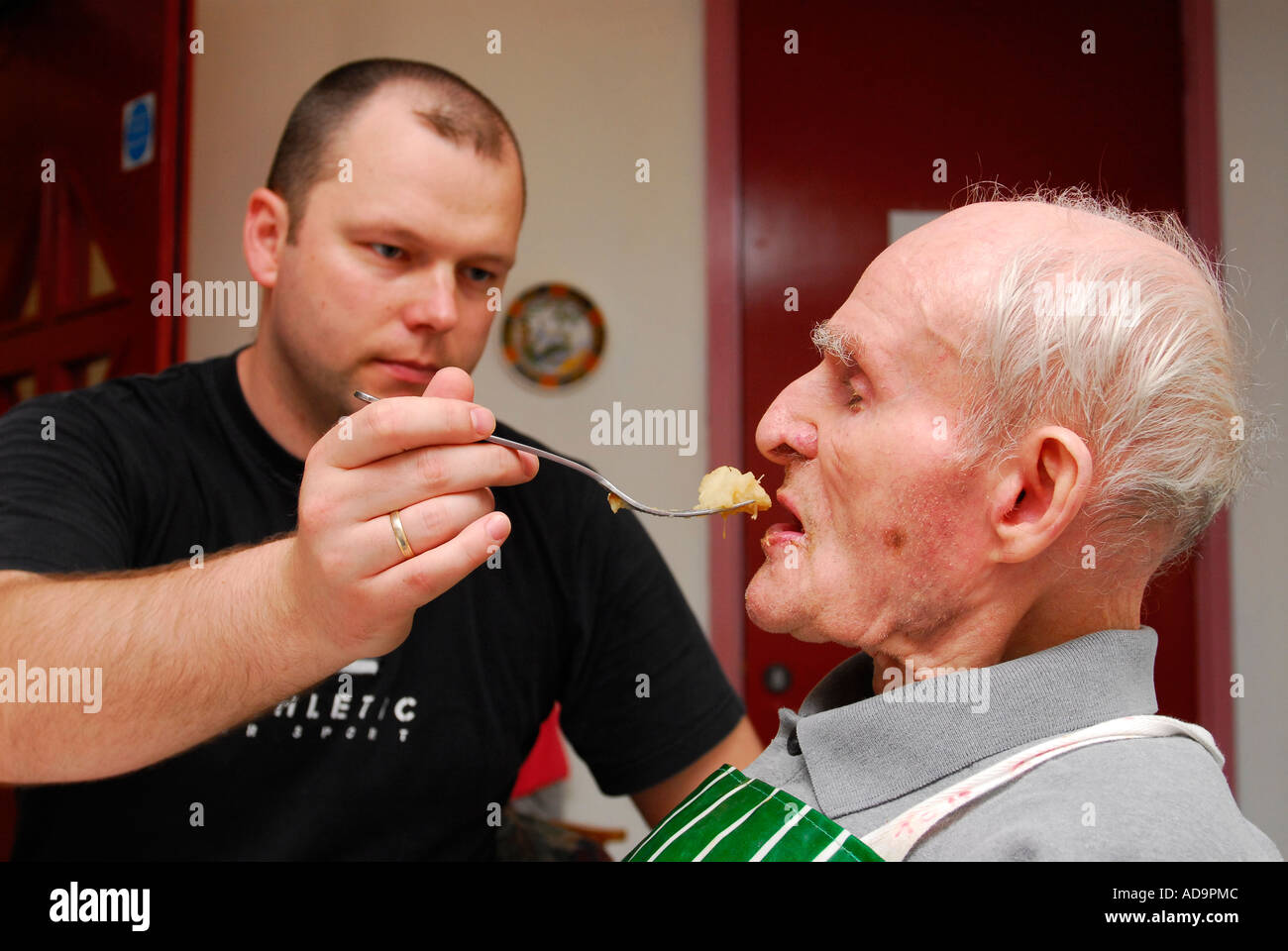 Member of care staff assisting elderly man with feeding in care home