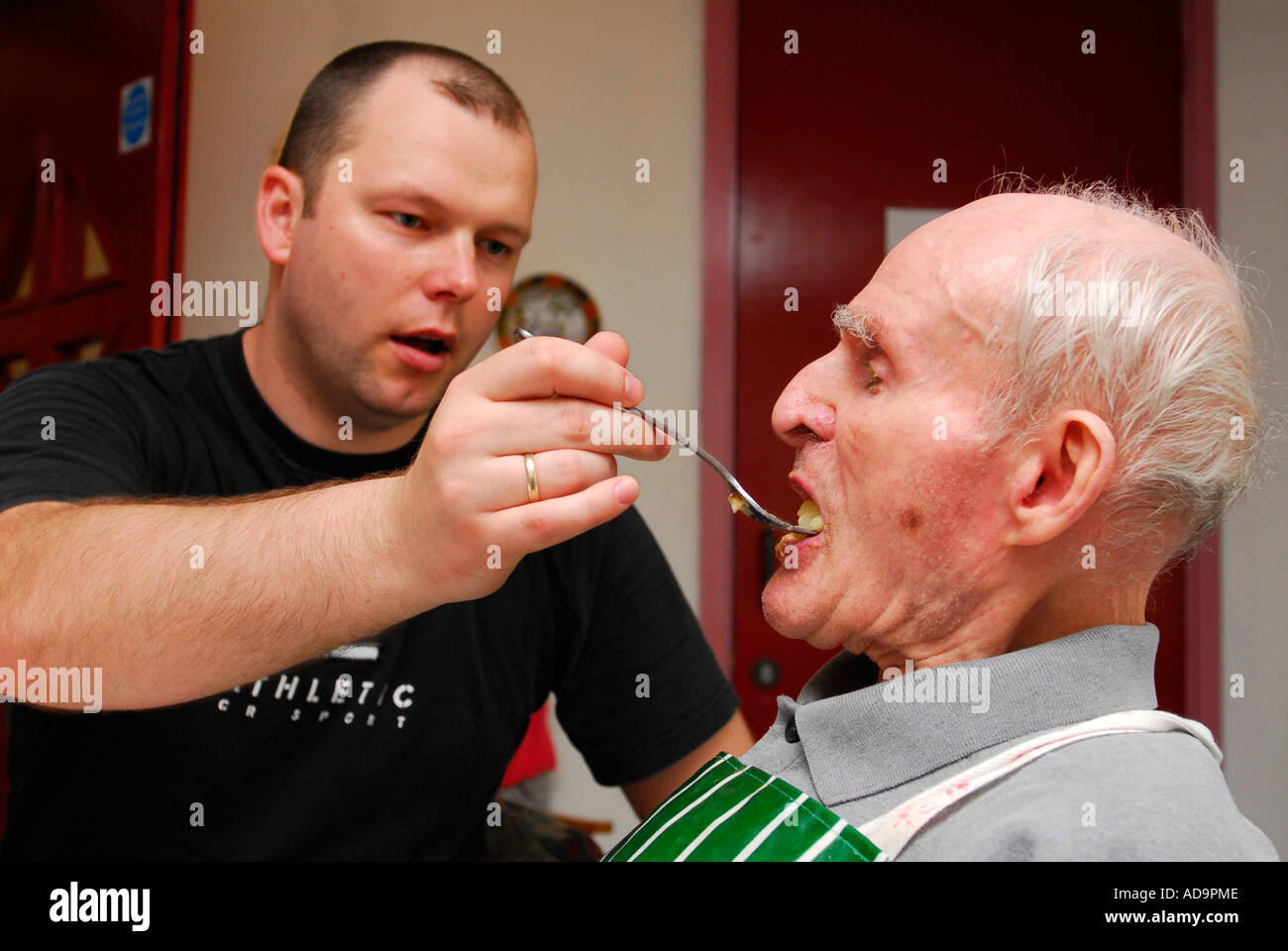 Member of care staff assisting elderly man with feeding in care home