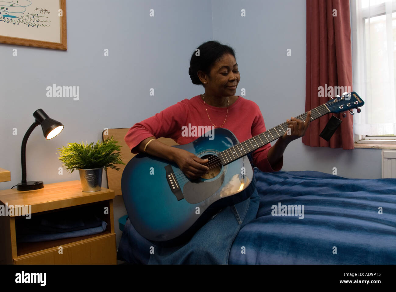 Mental health service user playing guitar in room London UK Stock Photo