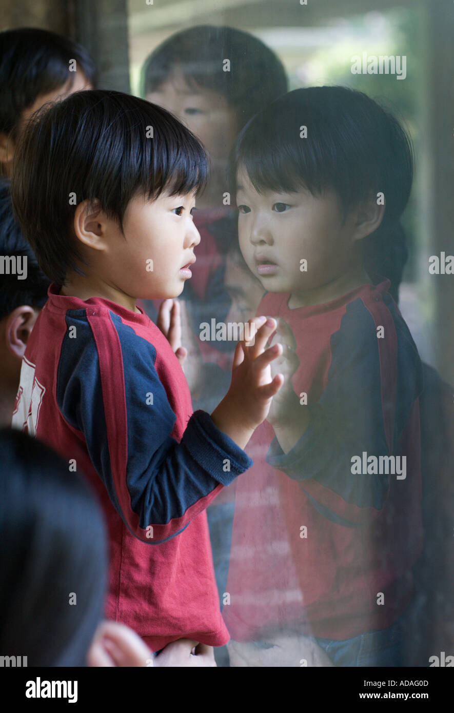 Young asian boy looking through window with his reflection in the window. Stock Photo