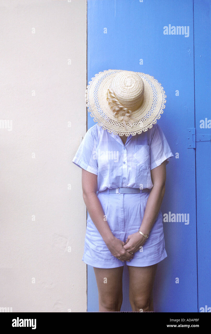 Woman With Head Down Against Blue And Tan Wall, Matching Her Outfit Stock Photo