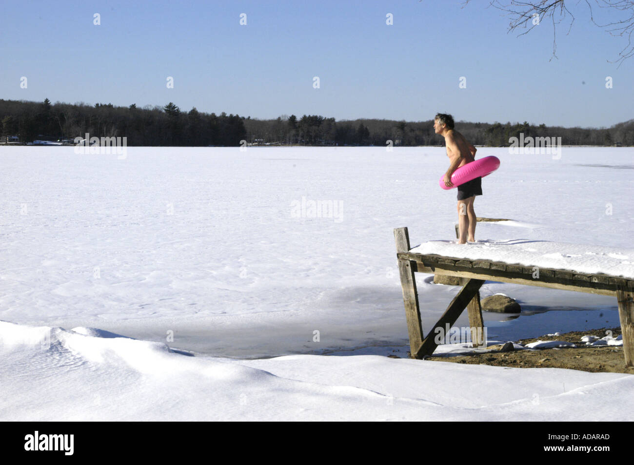 Man with inner tube ready to swim staring at frozen lake Stock Photo