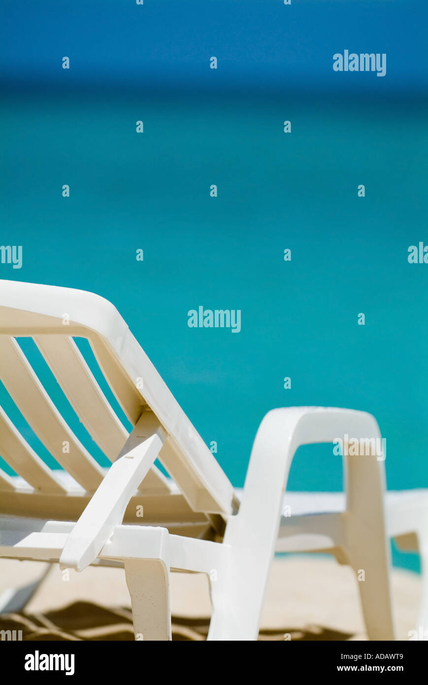 Empty white deck chair on a tropical beach with bright blue sea waters Stock Photo