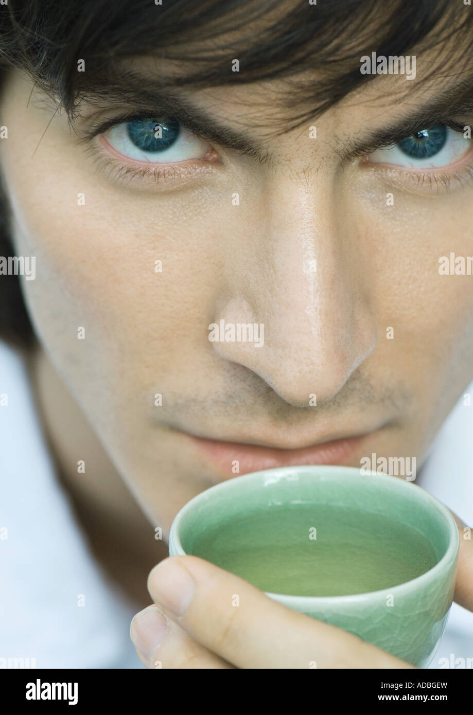 Man holding up cup of tea to mouth, looking at camera Stock Photo