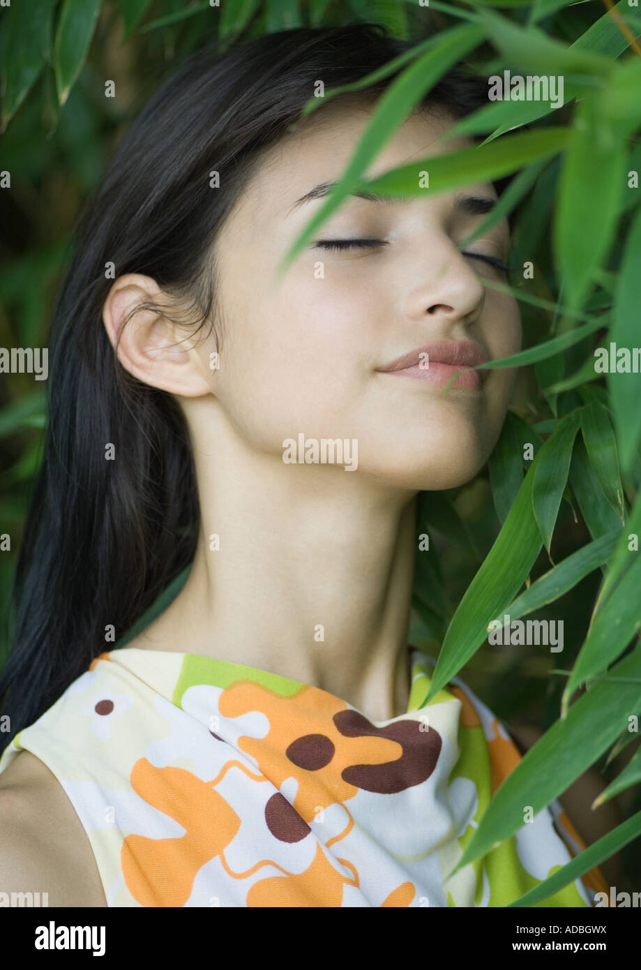 Woman standing in lush foliage, eyes closed, smiling Stock Photo