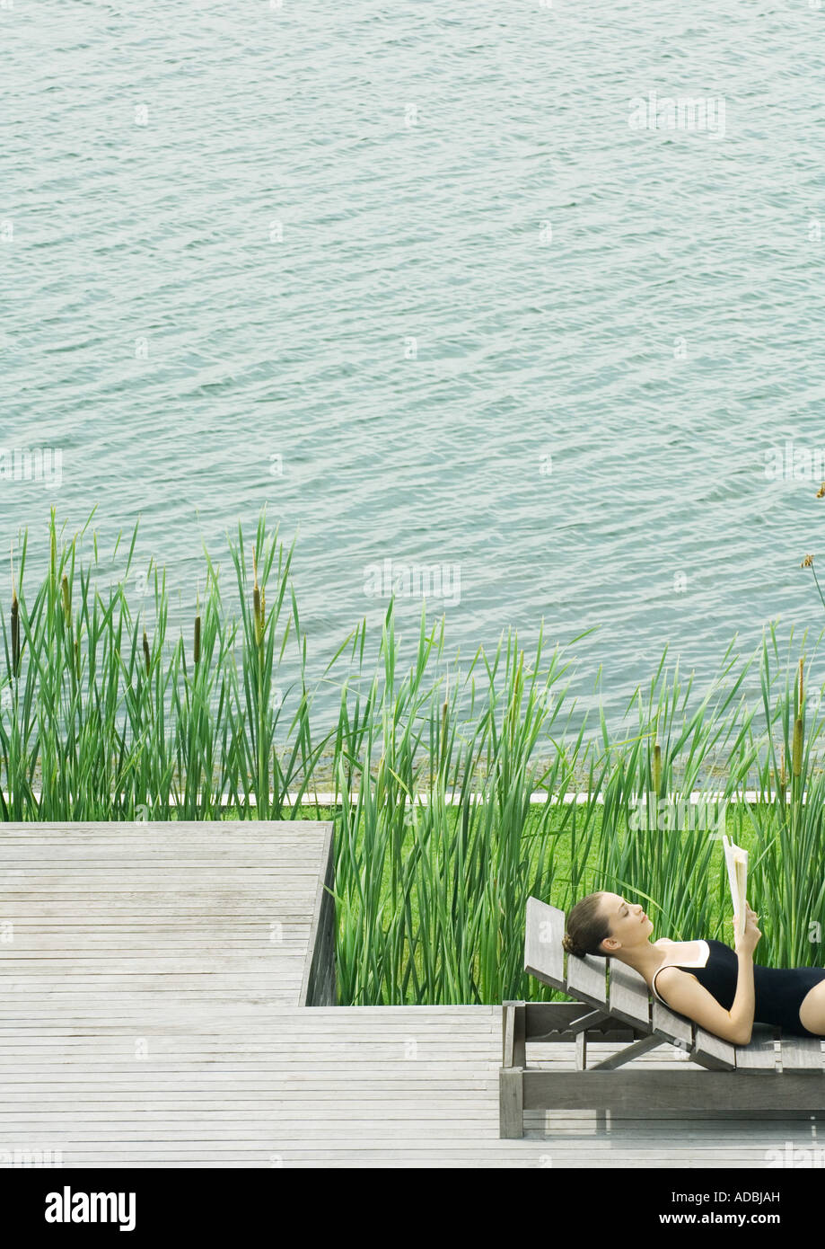 Woman reclining on lounge chair, reading, next to lake Stock Photo Alamy