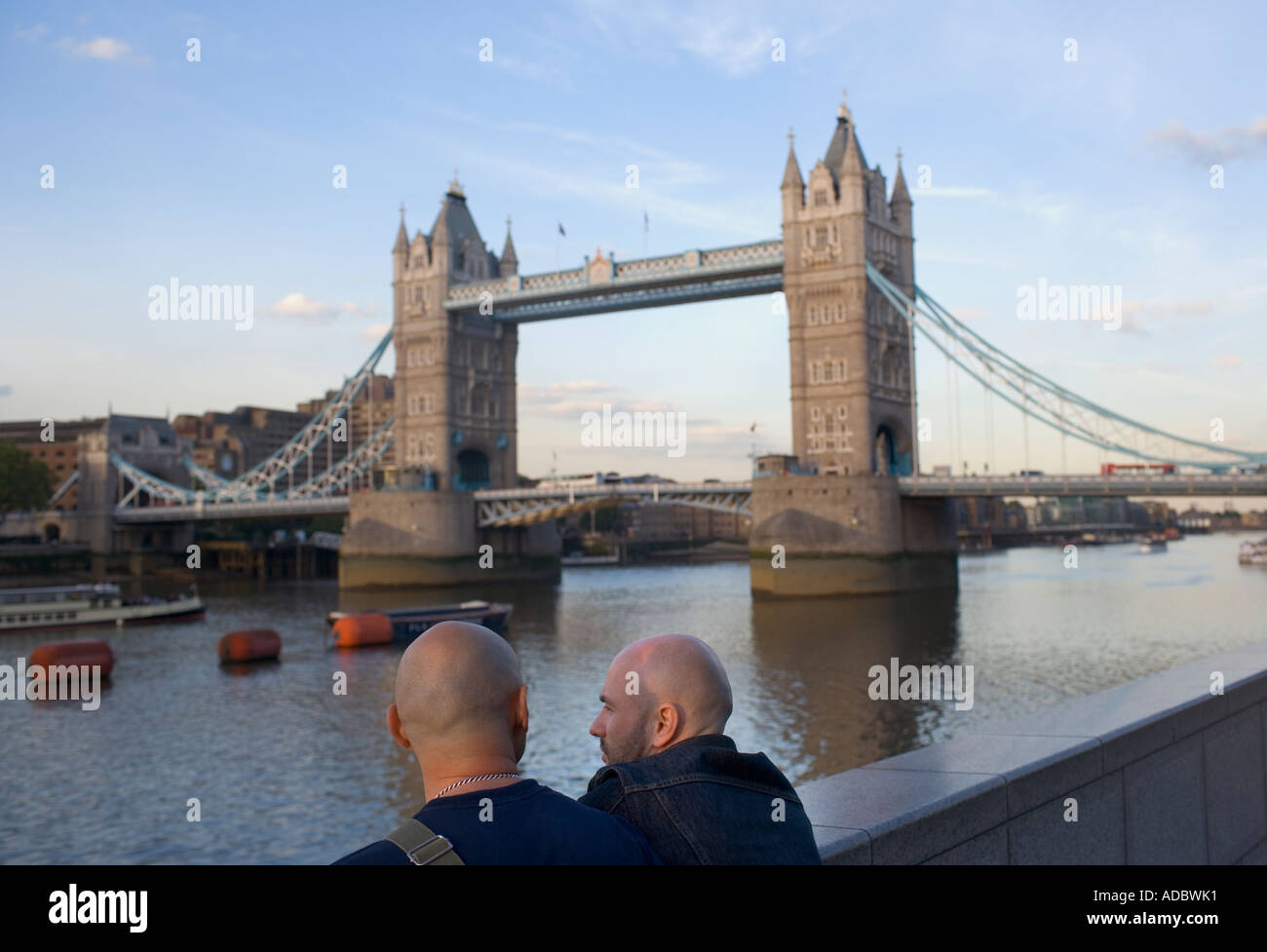 Two men with shaved heads along the River Thames in London next to the Tower Bridge Stock Photo