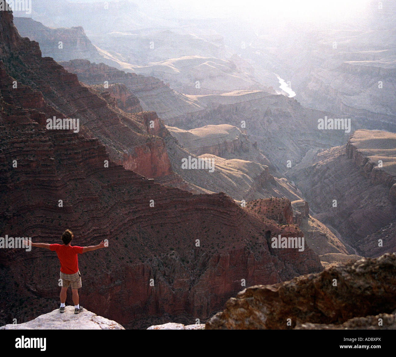 A man stands at the edge of the Grand Canyon and holds his arms out ...