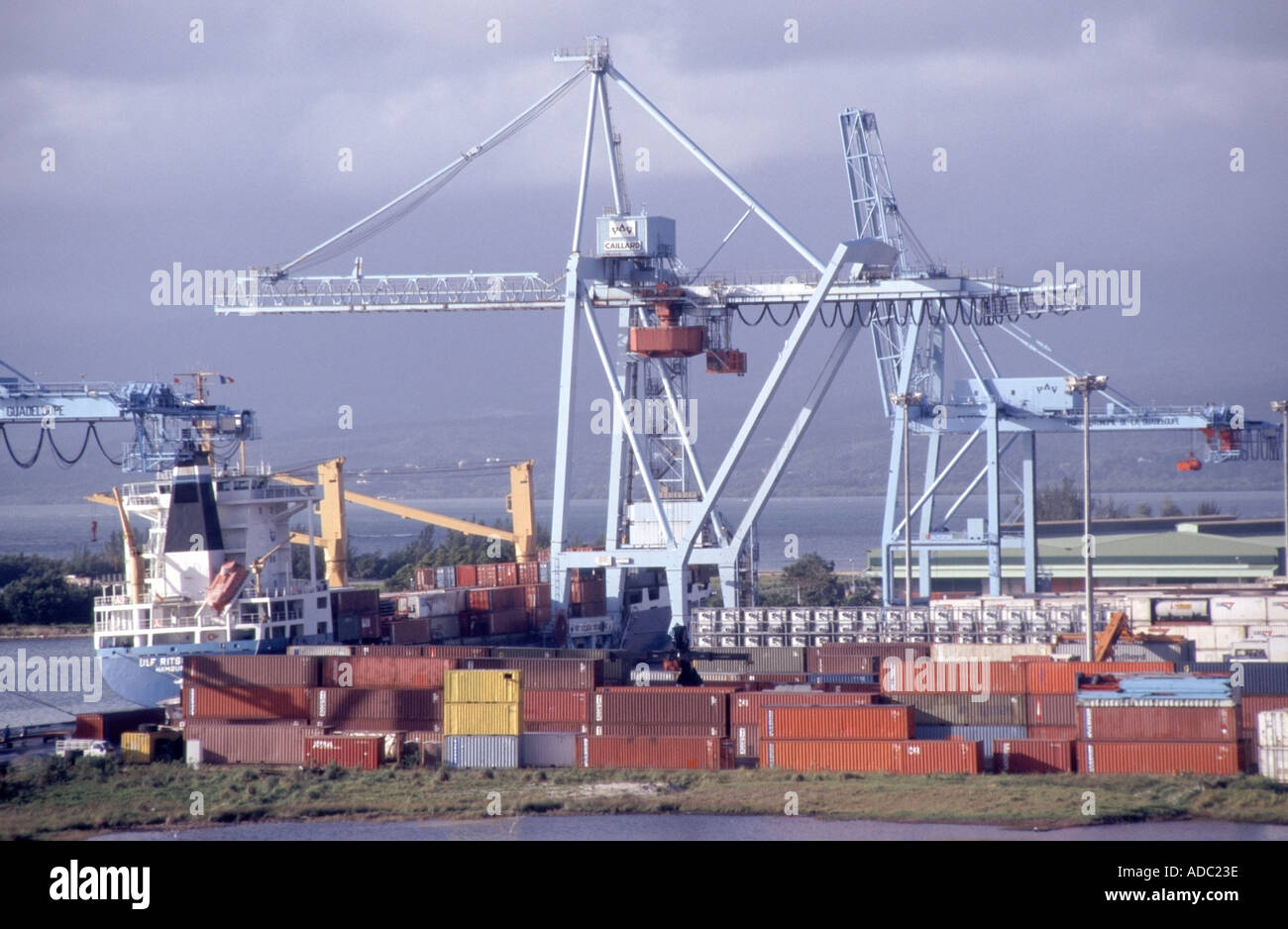 Pointe A Pitre dockside installations with small freighter berthed alongside cranes and container storage dump Stock Photo