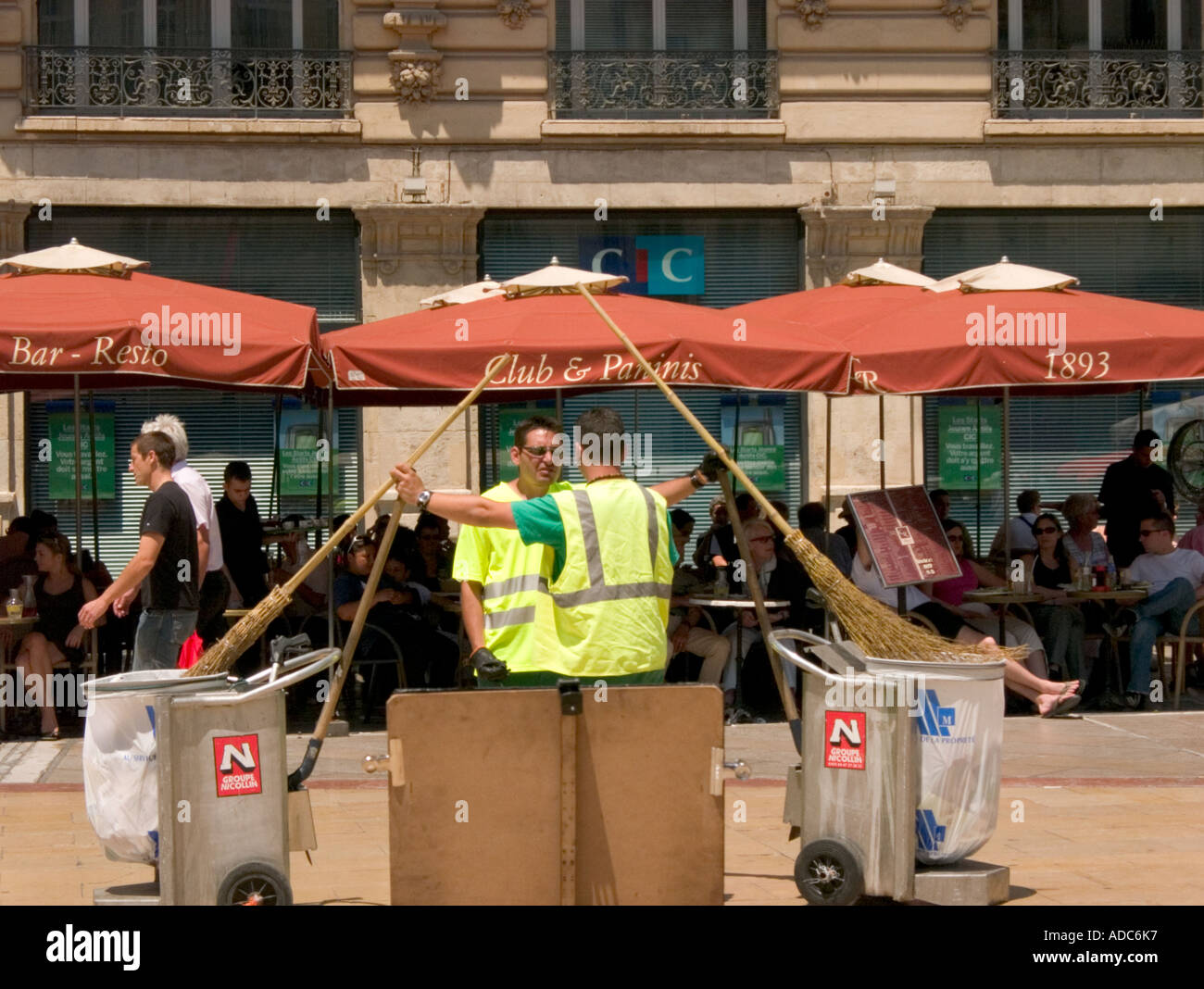 two street cleaners with brooms chat in the middle of a square in