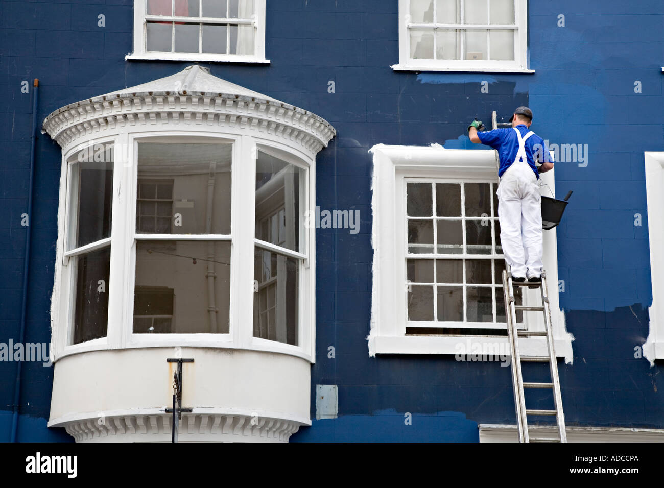 Main using a ladder painting outside wall of house Beaumaris Wales ...