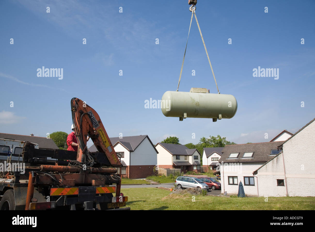 Large Calor gas tank being hoisted by a crane from a garden to a lorry against blue sky. UK Britain Stock Photo