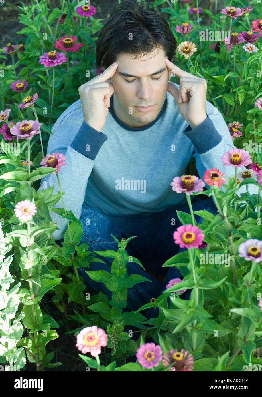 Man sitting in flowers, eyes closed and hands on temples Stock Photo