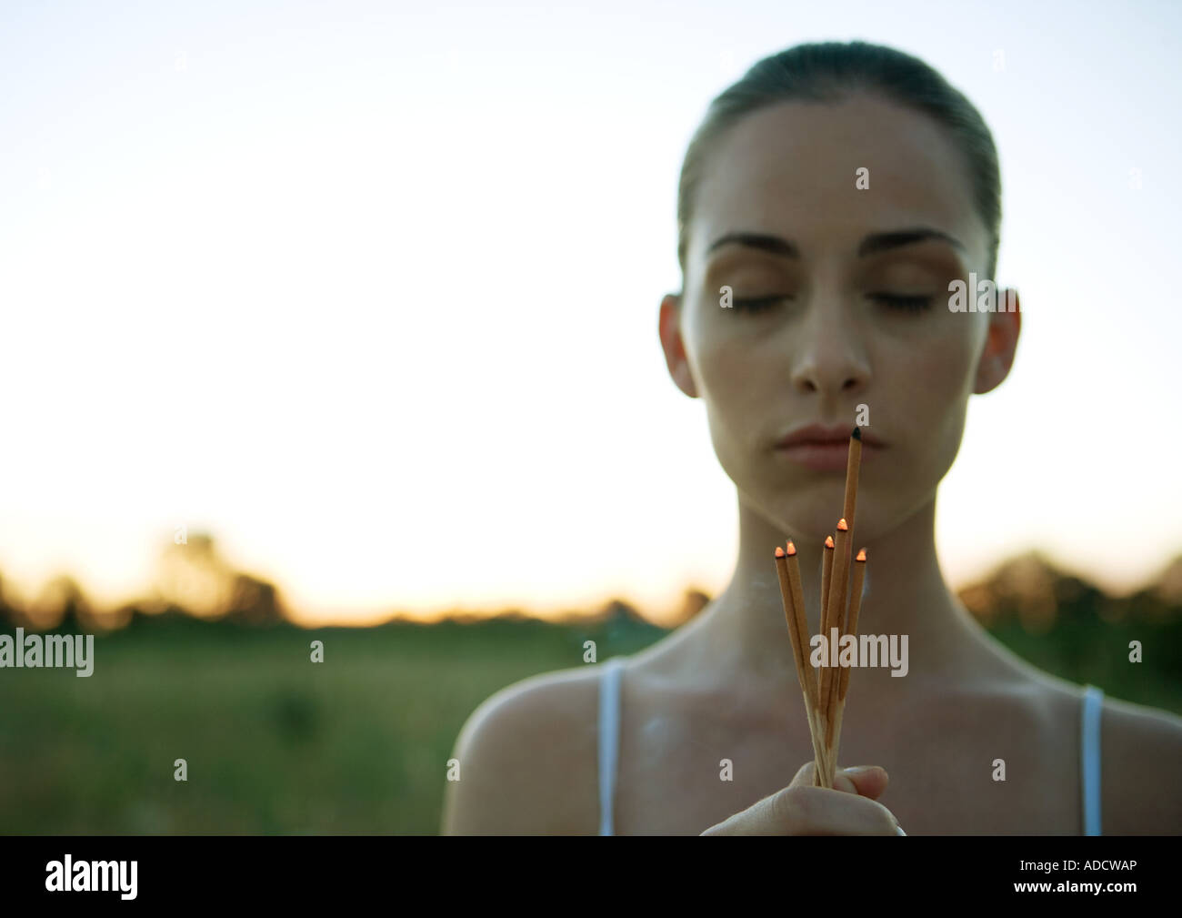 Woman holding bunch of incense, eyes closed, at sunset Stock Photo Alamy