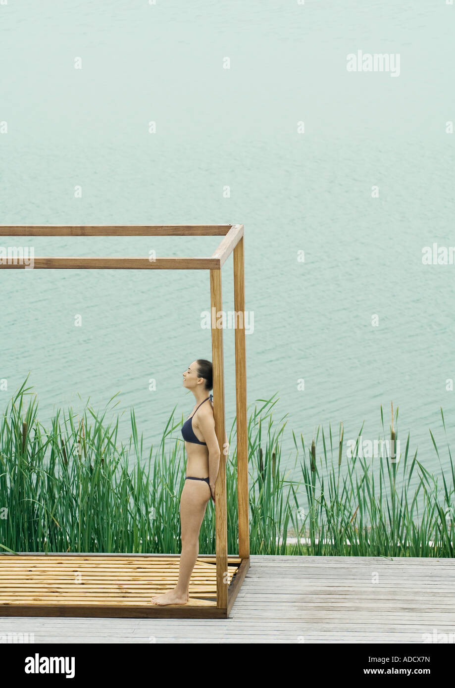 Woman wearing bikini, standing in wooden structure, near lake Stock Photo