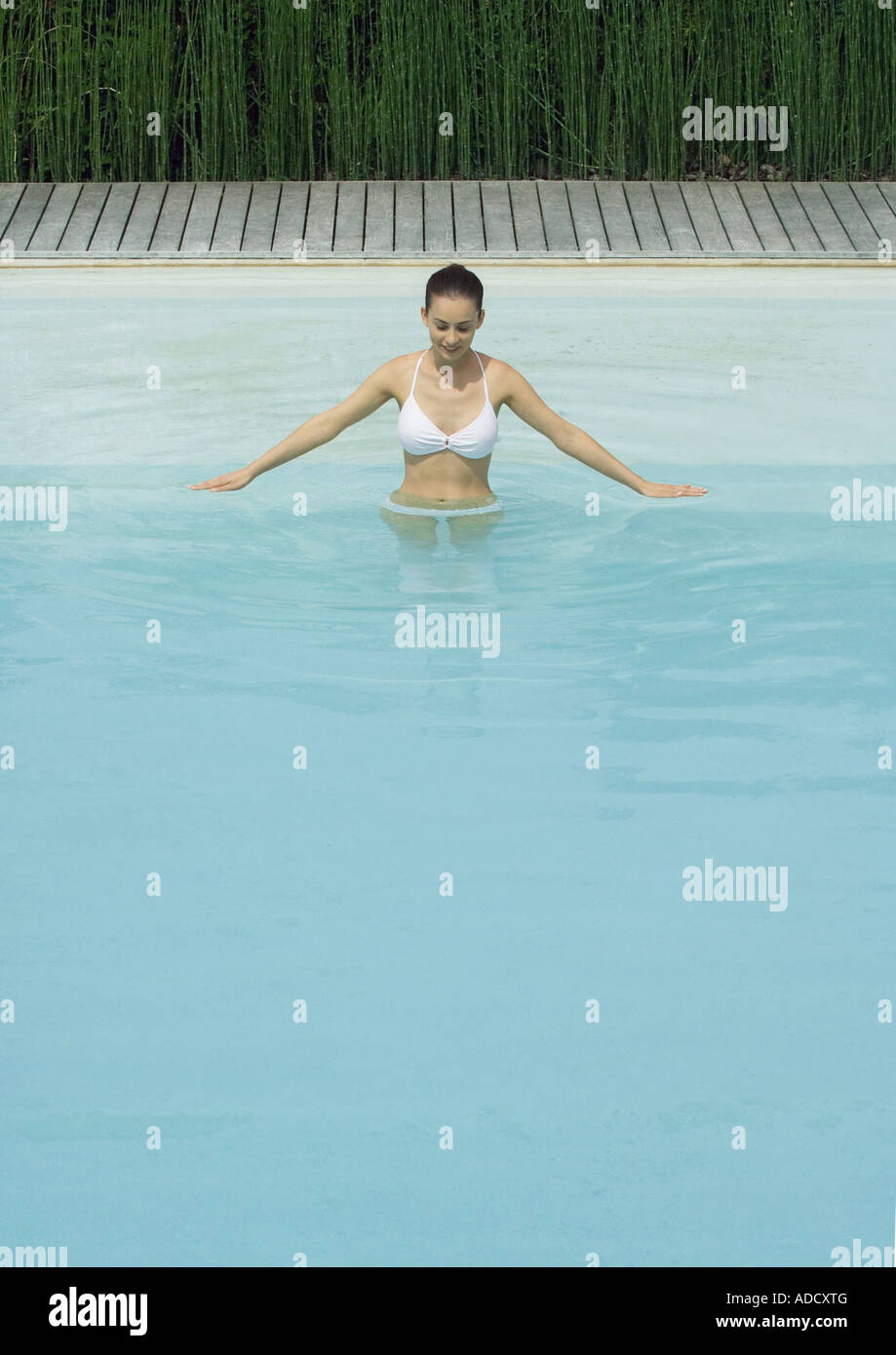 Woman standing in pool with arms out, looking down, smiling Stock Photo