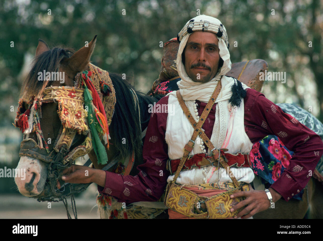 Horseman in traditional dress holding his horse which has eye defenders against the sun and dust Stock Photo