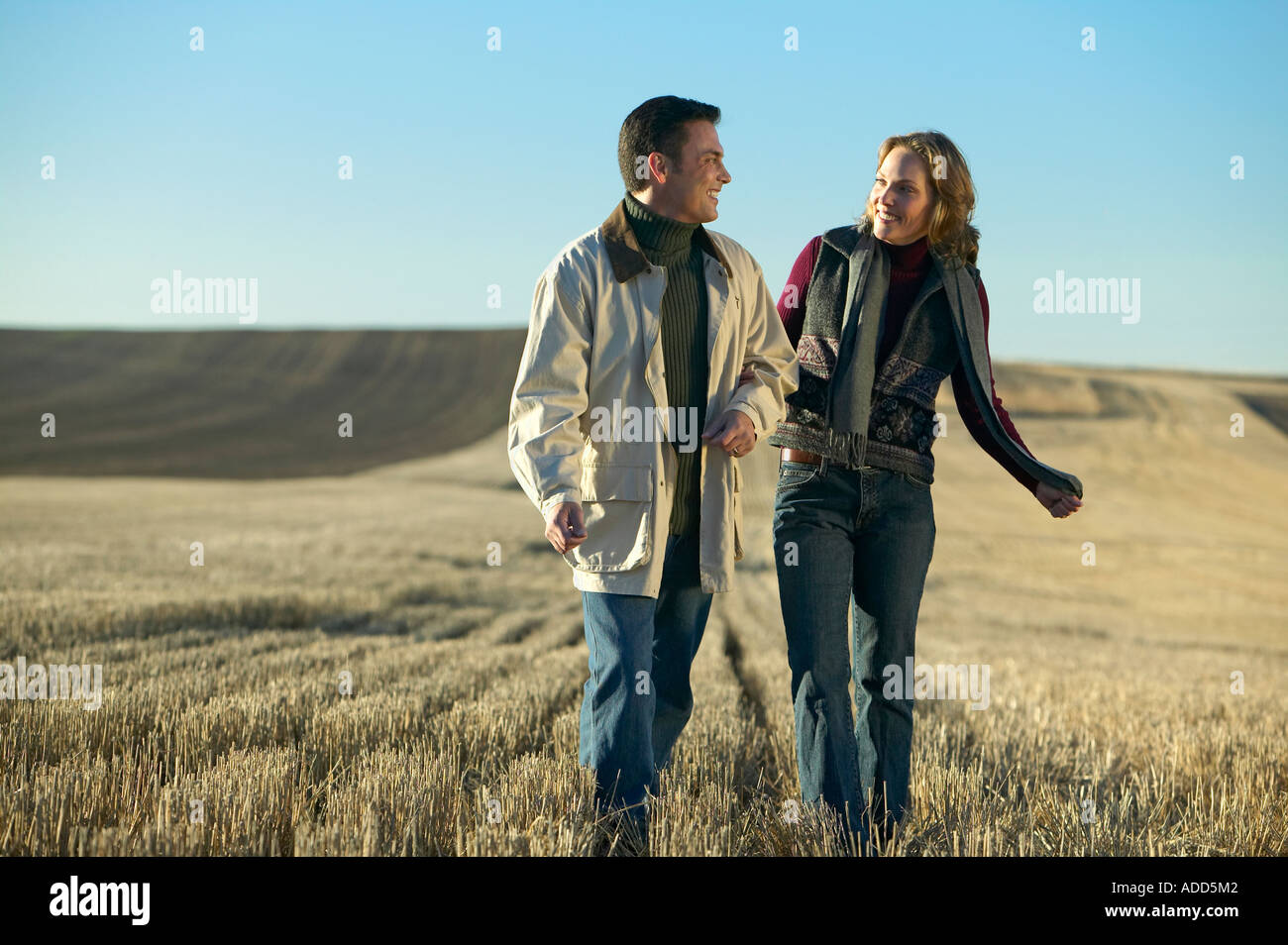 Couple laughing and walking through fields of cut grass in Fall Colorado early morning Stock Photo