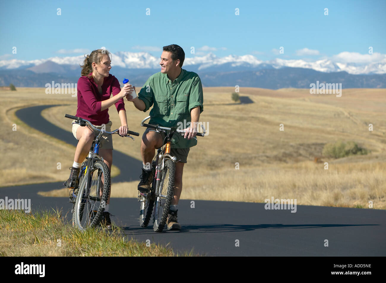 Smiling Middle aged couple riding bikes on a trail with mountain range in the background Stock Photo