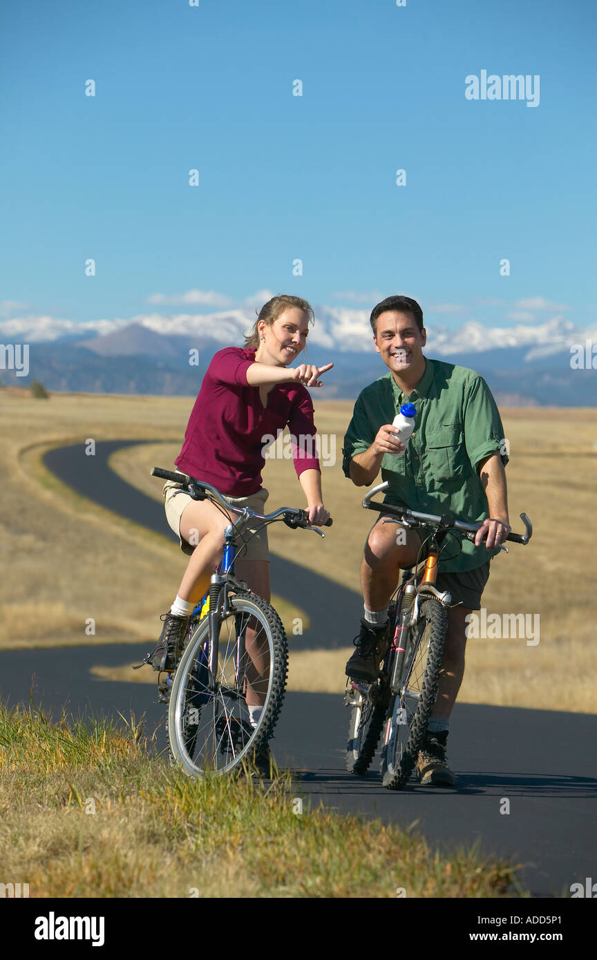 Smiling middle aged couple riding bikes on a trail with mountain range