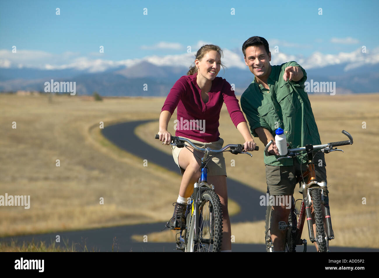 Smiling middle aged couple riding bikes on a trail with mountain range in the backgroundman points horizontal Stock Photo
