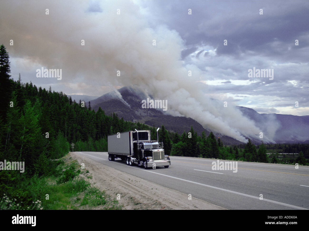 Articulated truck driving past the smoke of a forest fire in Canada Stock Photo