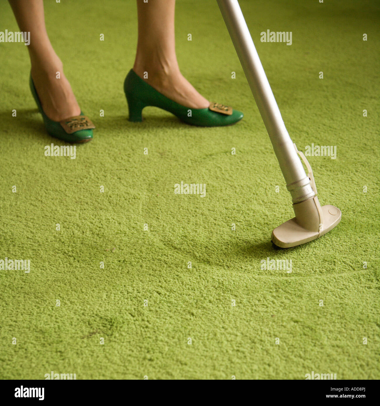 Close up of Caucasian female feet with vacuum extension against green retro carpet Stock Photo