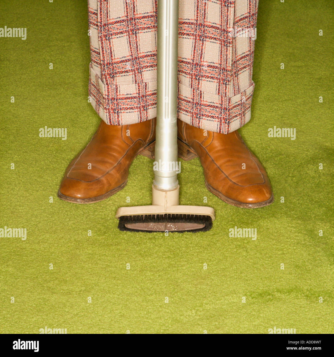 Close up of Caucasian male legs in plaid pants with vacuum extension standing on green retro carpet Stock Photo