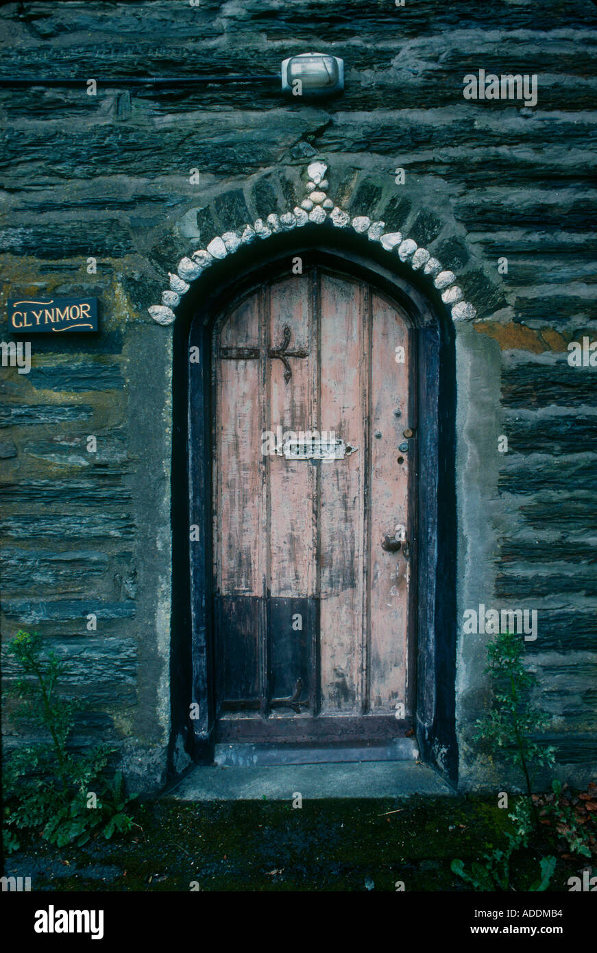 Pink faded arched front door decorated with shells on cottage made of