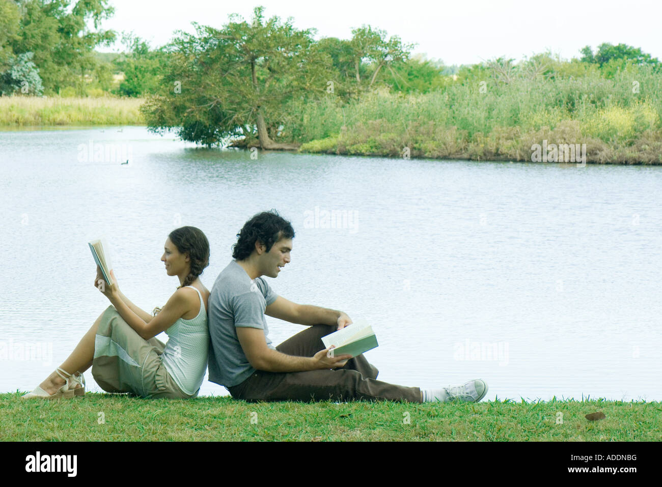 Couple sitting by lake, back to back, reading Stock Photo