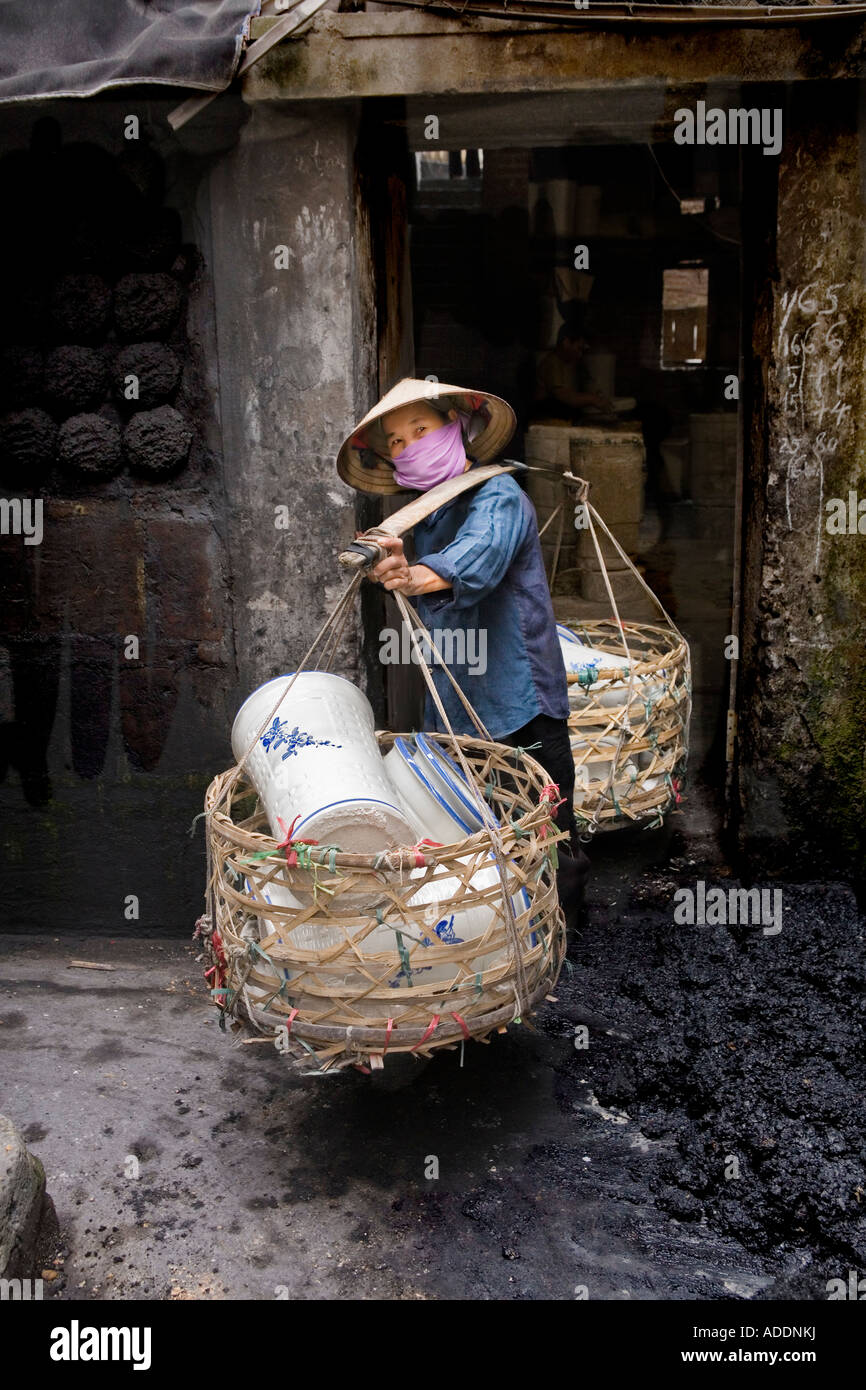 Vietnamese woman carries a yoke heavily loaded with baskets of large ceramic pots Stock Photo