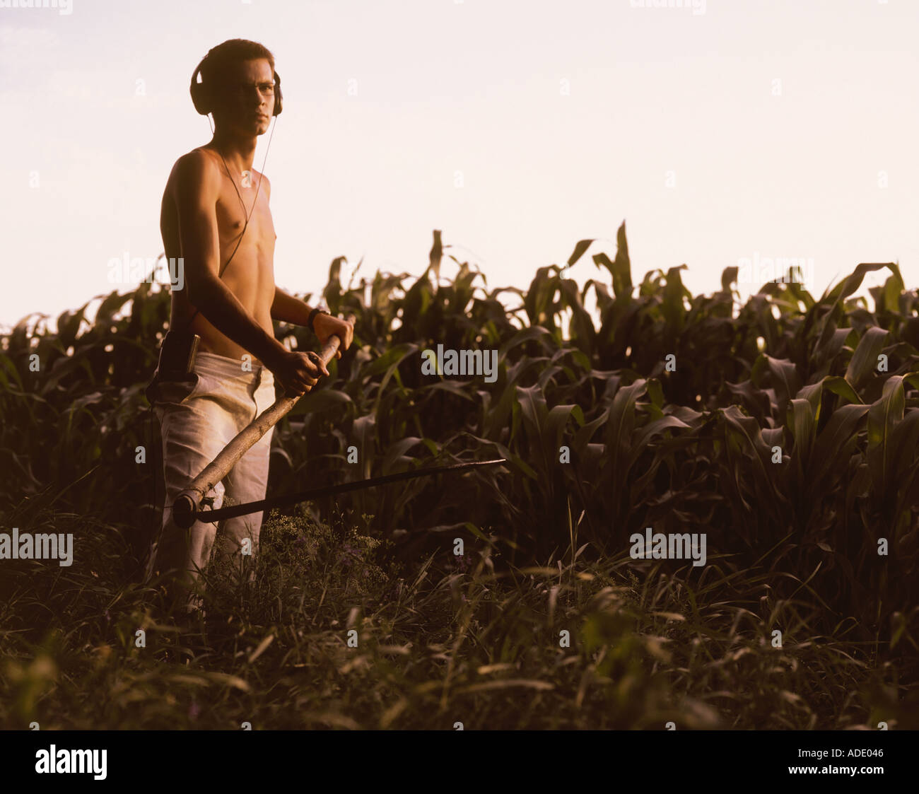 Shirtless young man in headphones mowing grass with scythe Stock Photo -  Alamy