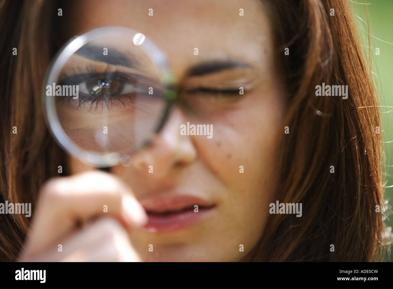 Young woman looks  through a magnifying glass with one eye © Peter Schatz/Alamy Stock Photo