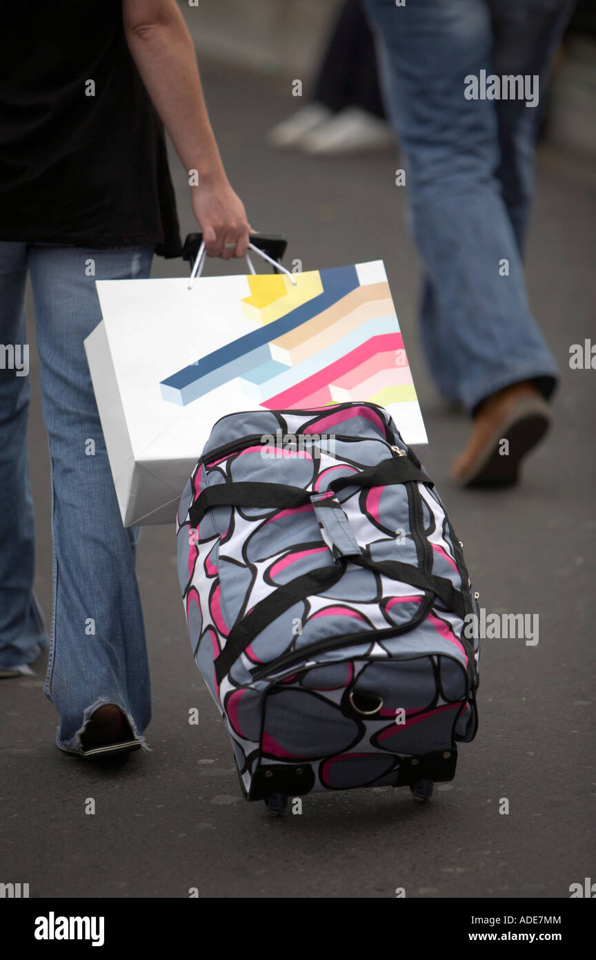 woman in jeans pulling brightly coloured luggage and up market shopping bag along street in dublin Stock Photo