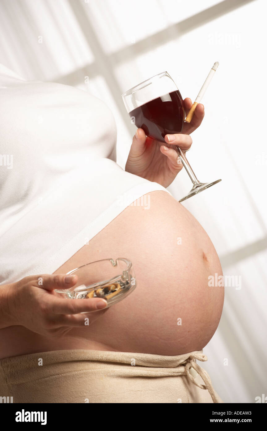 ATTRACTIVE HEALTHY YOUNG PREGNANT WOMAN SMOKING CIGARETTE AND DRINKING GLASS OF RED WINE Stock