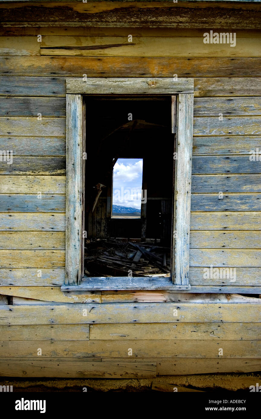 window in an old wood building looking though to the window on the other side of the building.  Blue sky and mountains in second Stock Photo
