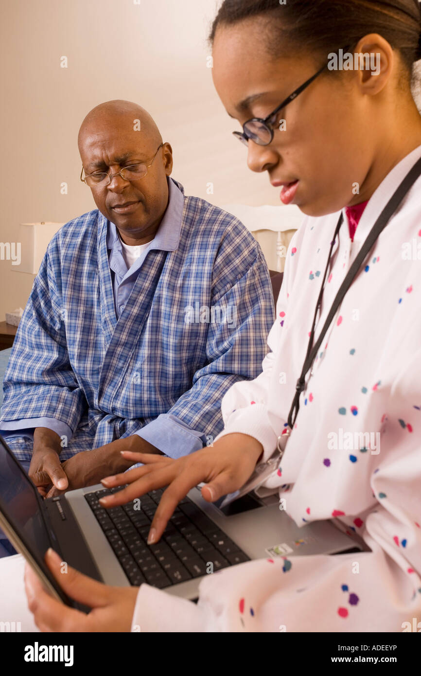 Nurse visits elderly patient, inputs data using laptop computer. Stock Photo