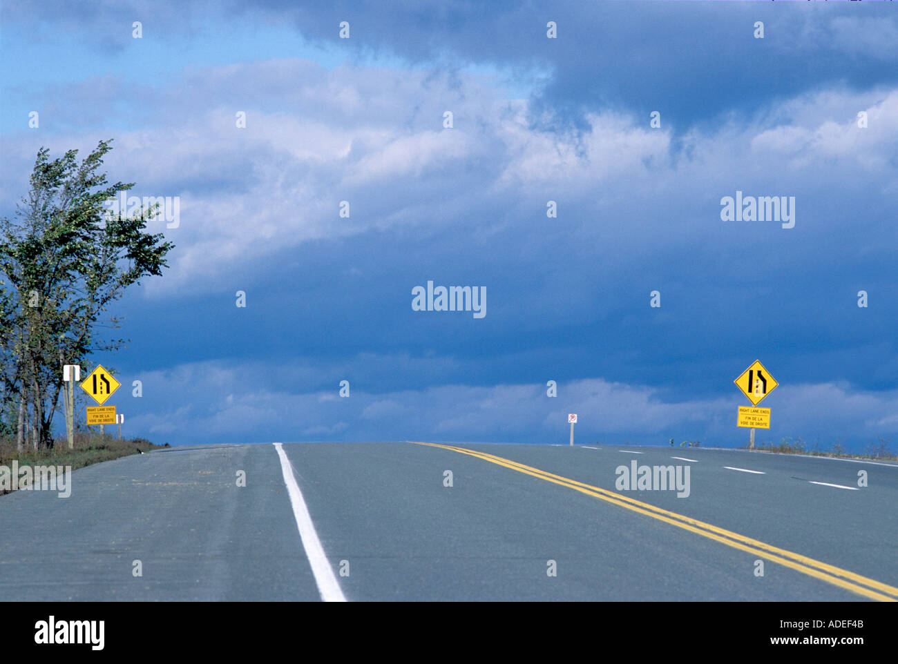 open road over crest of hill with storm clouds in the background while