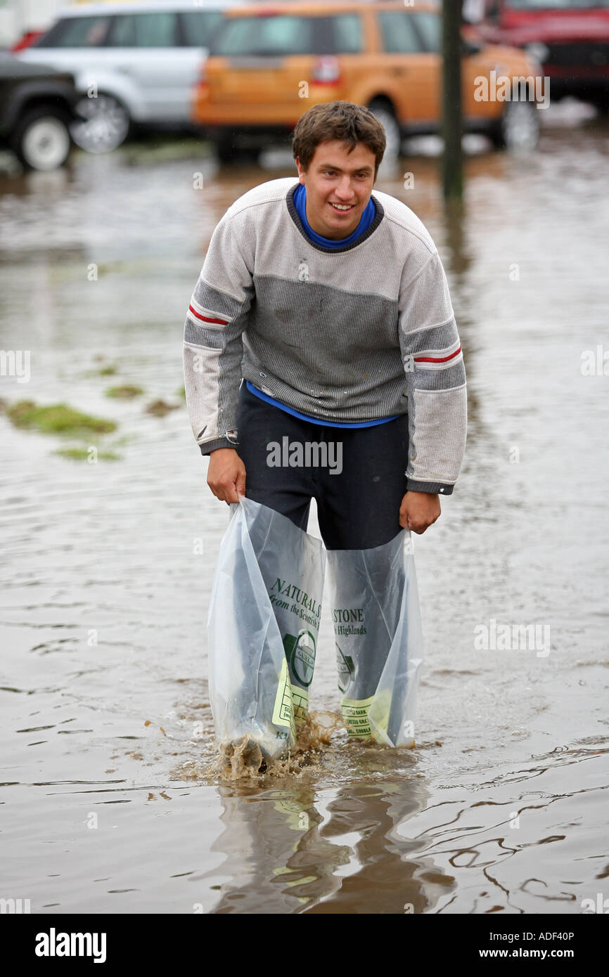 Boy splashes through flooded field with plastic bags on his feet after heavy rain near Turriff, Aberdeenshire, Scotland, UK Stock Photo