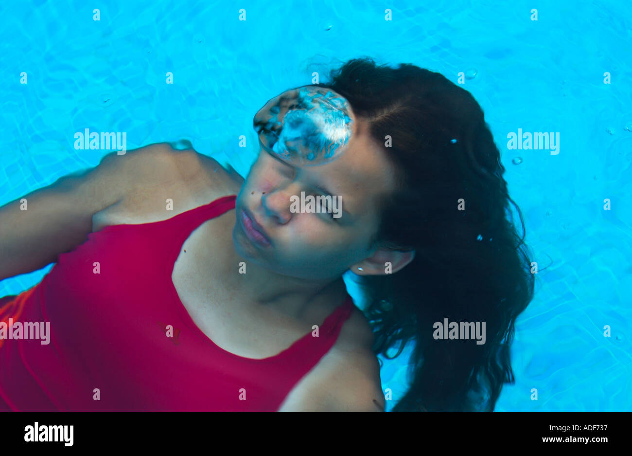 Teenage Girl Wearing Red Bathing Suit Floats In Swimming Pool Just Below The Water Surface And