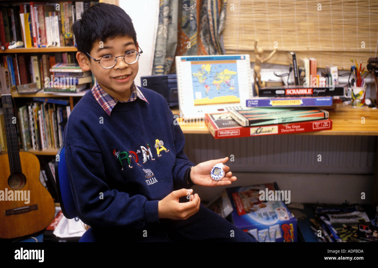 Young boy sitting in his bedroom at his desk holding a tamagotchi computer top with games in background. Stock Photo