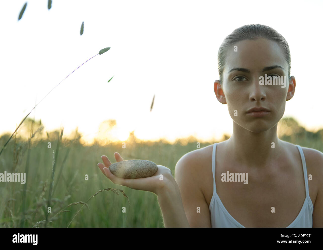 Woman sitting in field, holding stone in hand Stock Photo