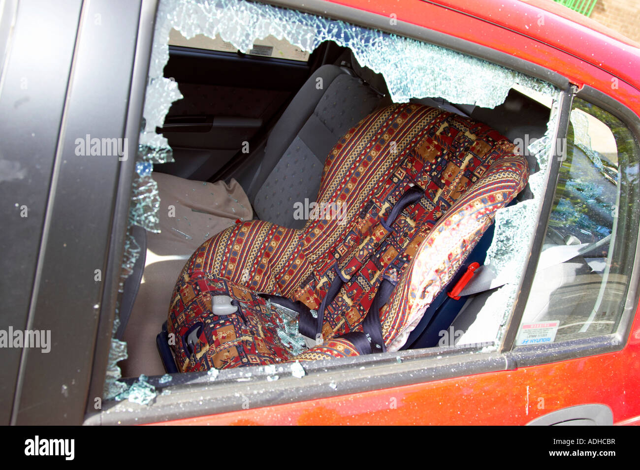 smashed rear passenger window of red hyundai car with childs car seat