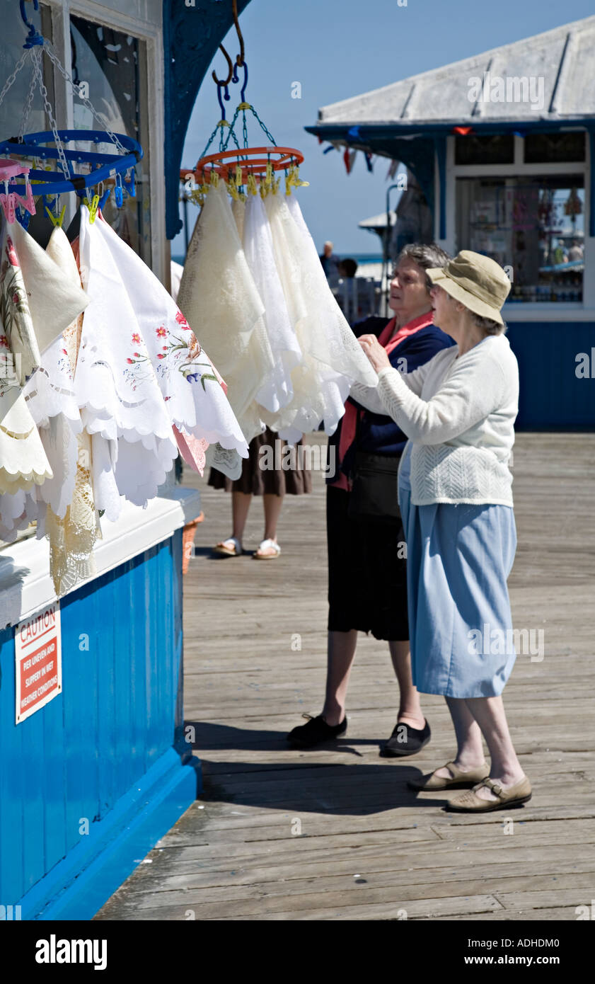 Lace tablecloths on sale on pier stall with two ladies inspecting samples Llandudno Wales UK Stock Photo